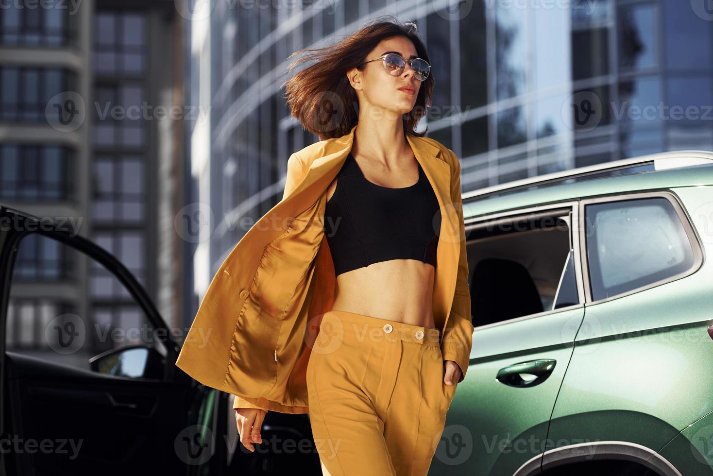 Young fashionable woman in burgundy colored coat at daytime with her car photo