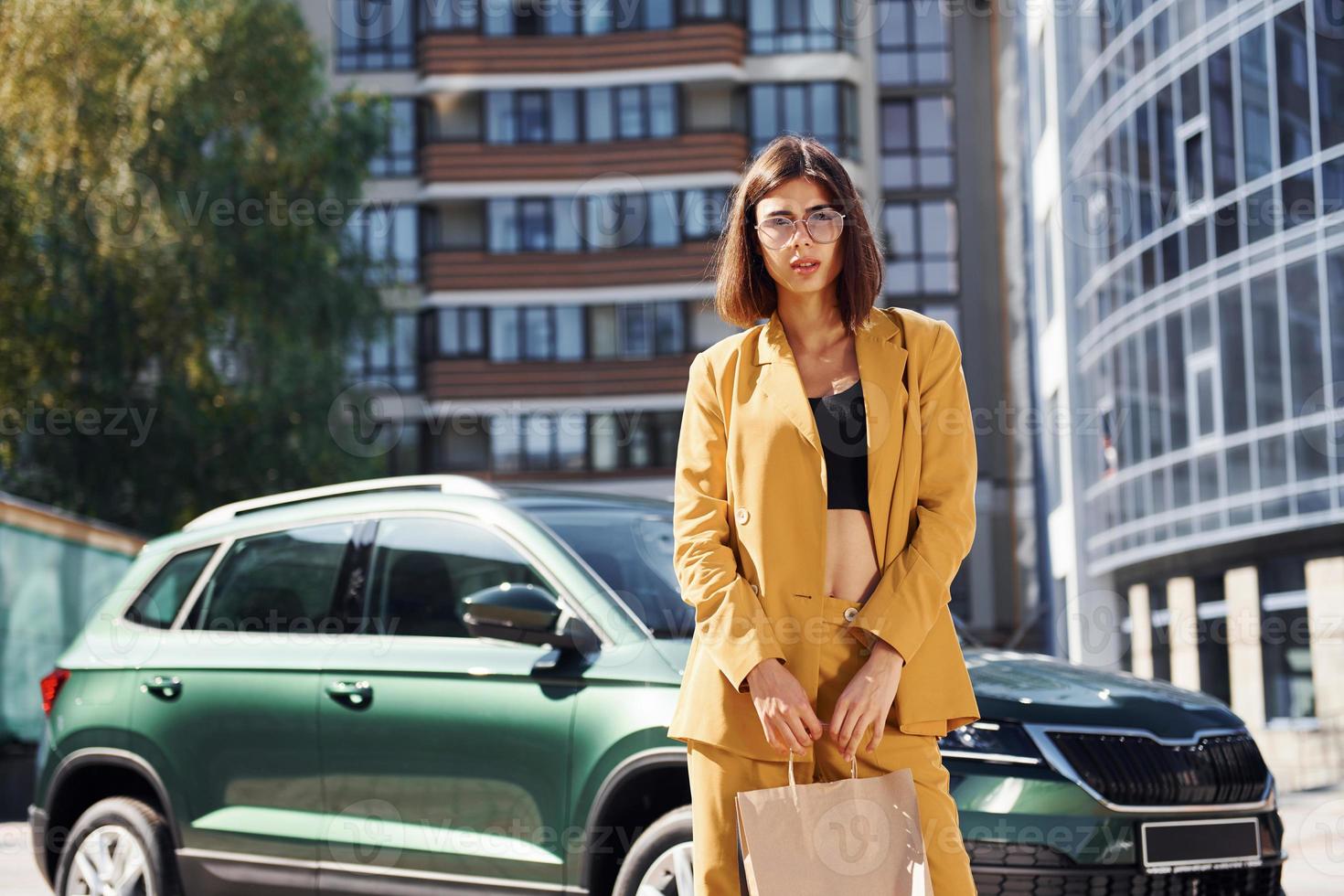 Young fashionable woman in burgundy colored coat at daytime with her car photo