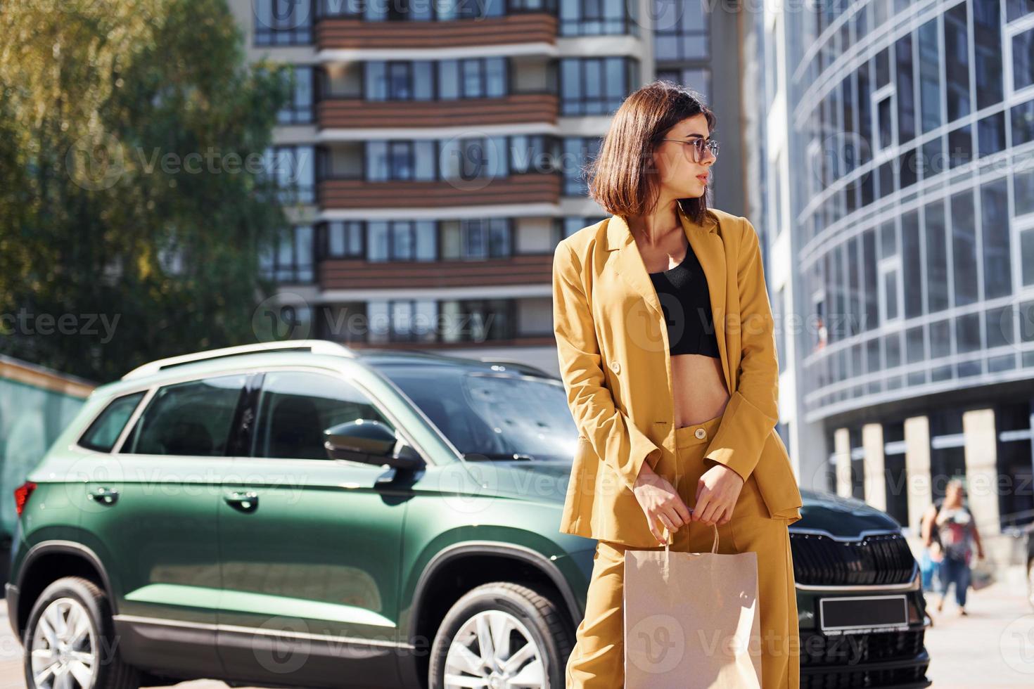 Young fashionable woman in burgundy colored coat at daytime with her car photo