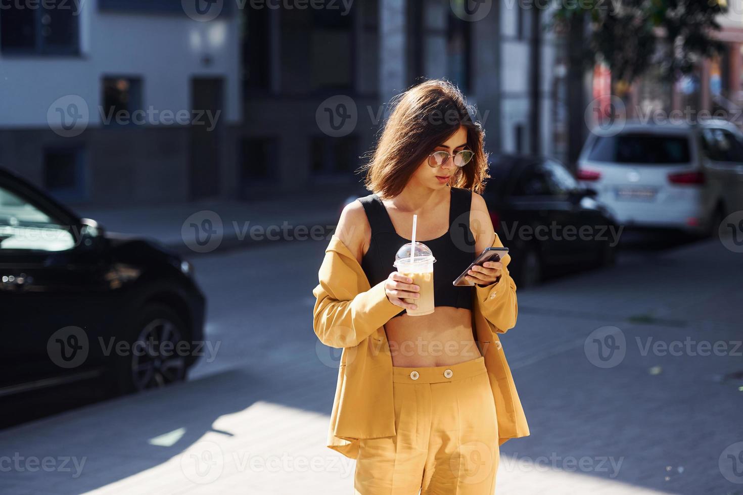 Coffee break. Young fashionable woman in burgundy colored coat at daytime with her car photo