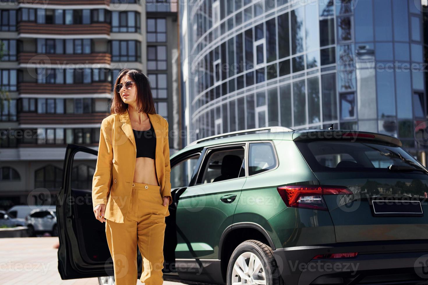 Walks forward from automobile. Young fashionable woman in burgundy colored coat at daytime with her car photo