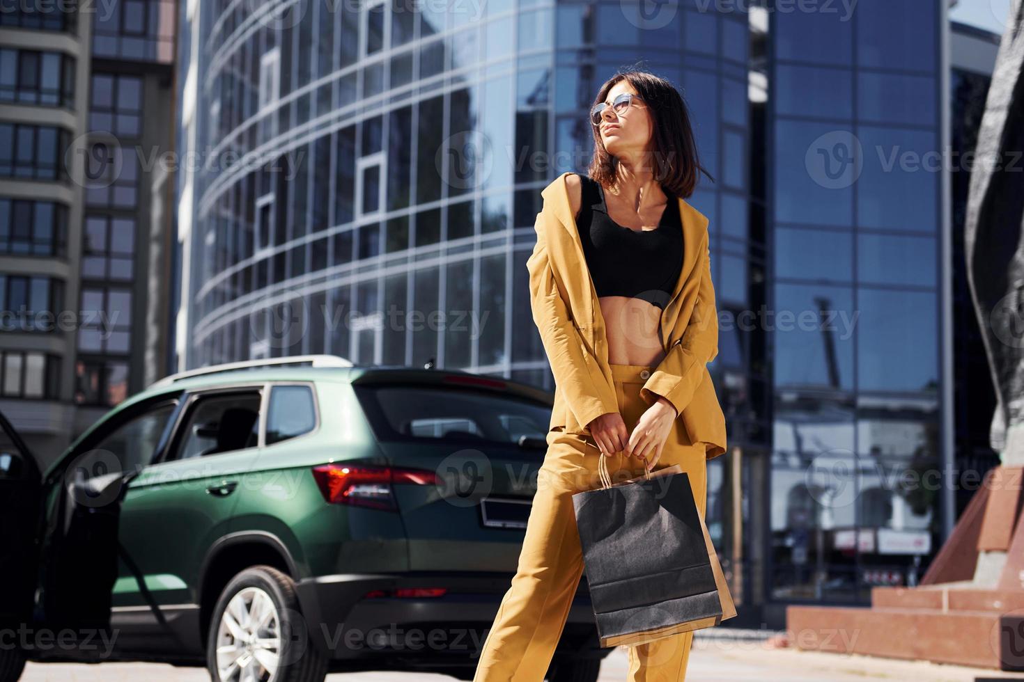 Modern business building at background. Young fashionable woman in burgundy colored coat at daytime with her car photo