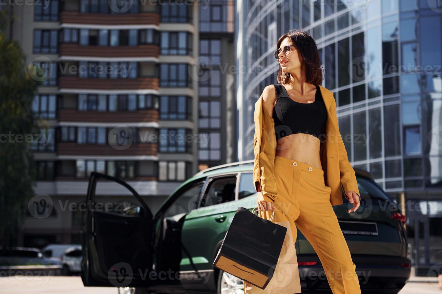 Modern business building at background. Young fashionable woman in burgundy colored coat at daytime with her car photo