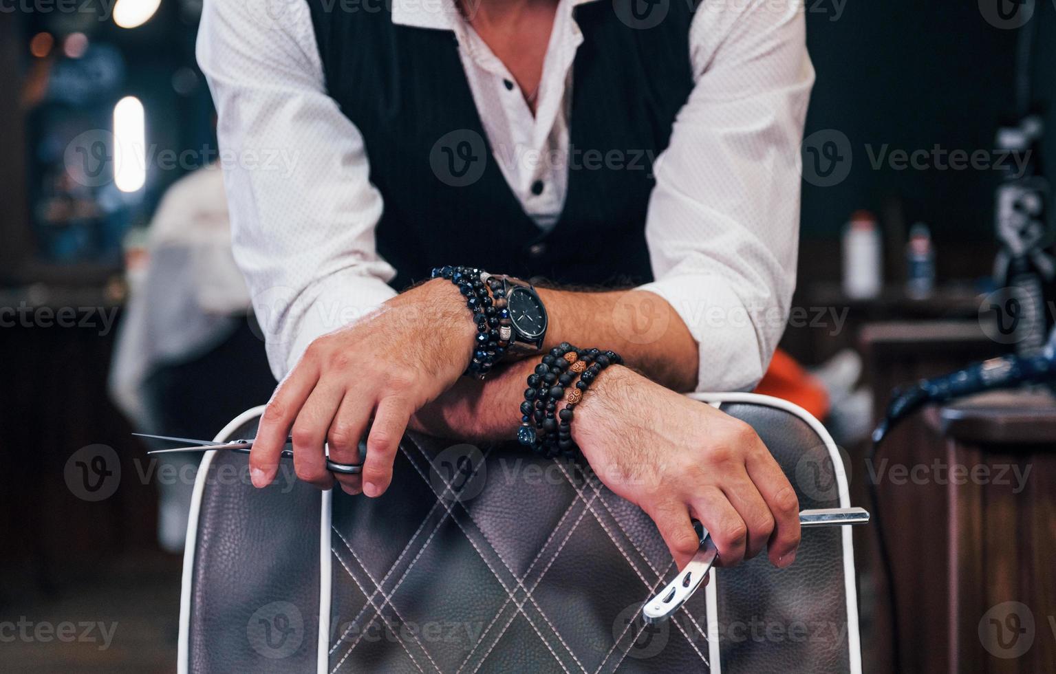 Close up view of man in luxury clothes that standing indoors in barbershop with scissors photo