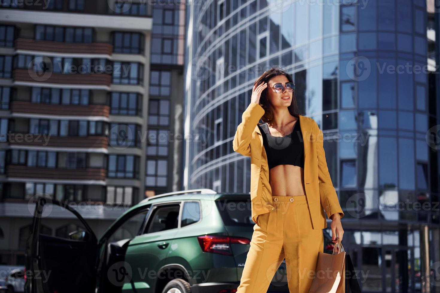 Modern business building at background. Young fashionable woman in burgundy colored coat at daytime with her car photo