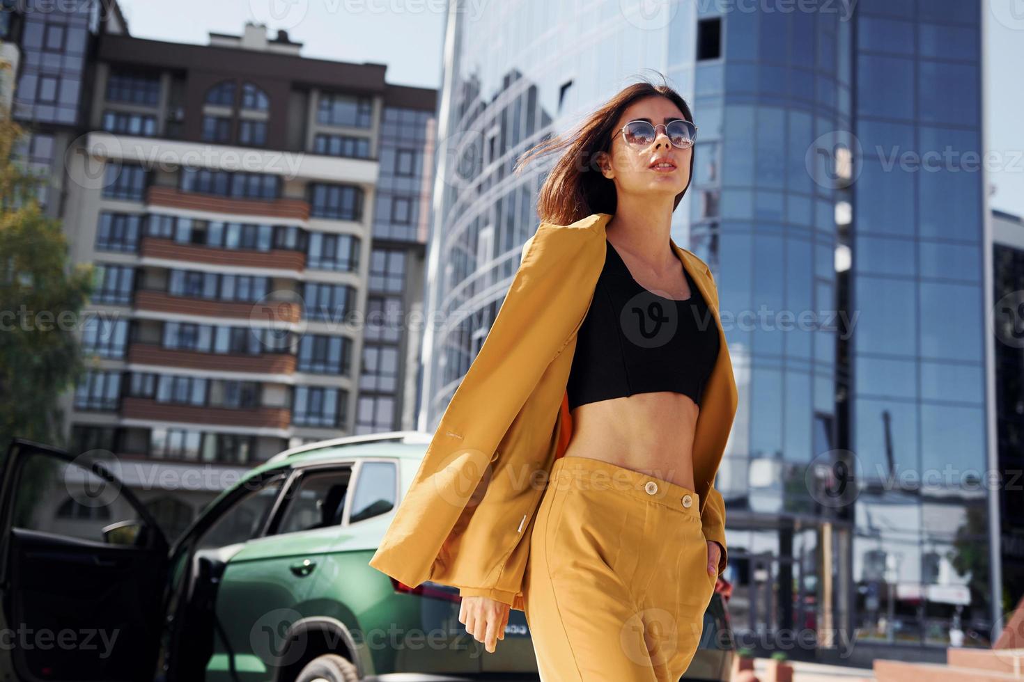 Walks forward from automobile. Young fashionable woman in burgundy colored coat at daytime with her car photo