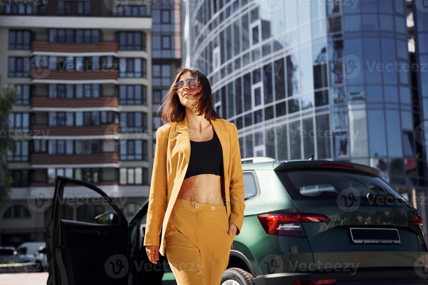 Walks forward from automobile. Young fashionable woman in burgundy colored coat at daytime with her car photo