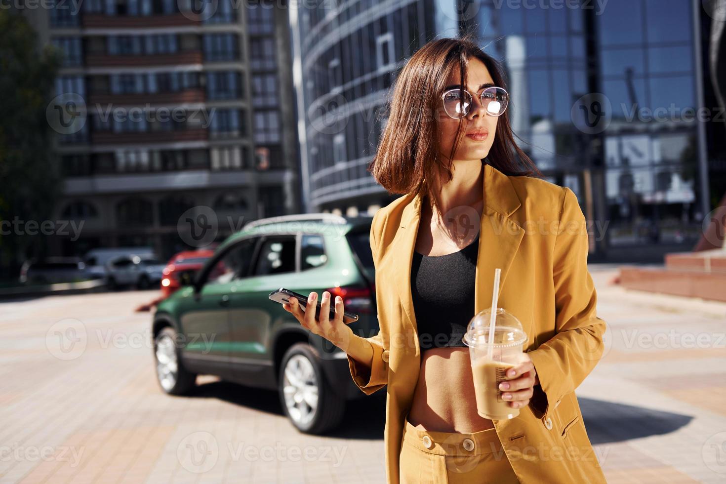 Modern business building at background. Young fashionable woman in burgundy colored coat at daytime with her car photo
