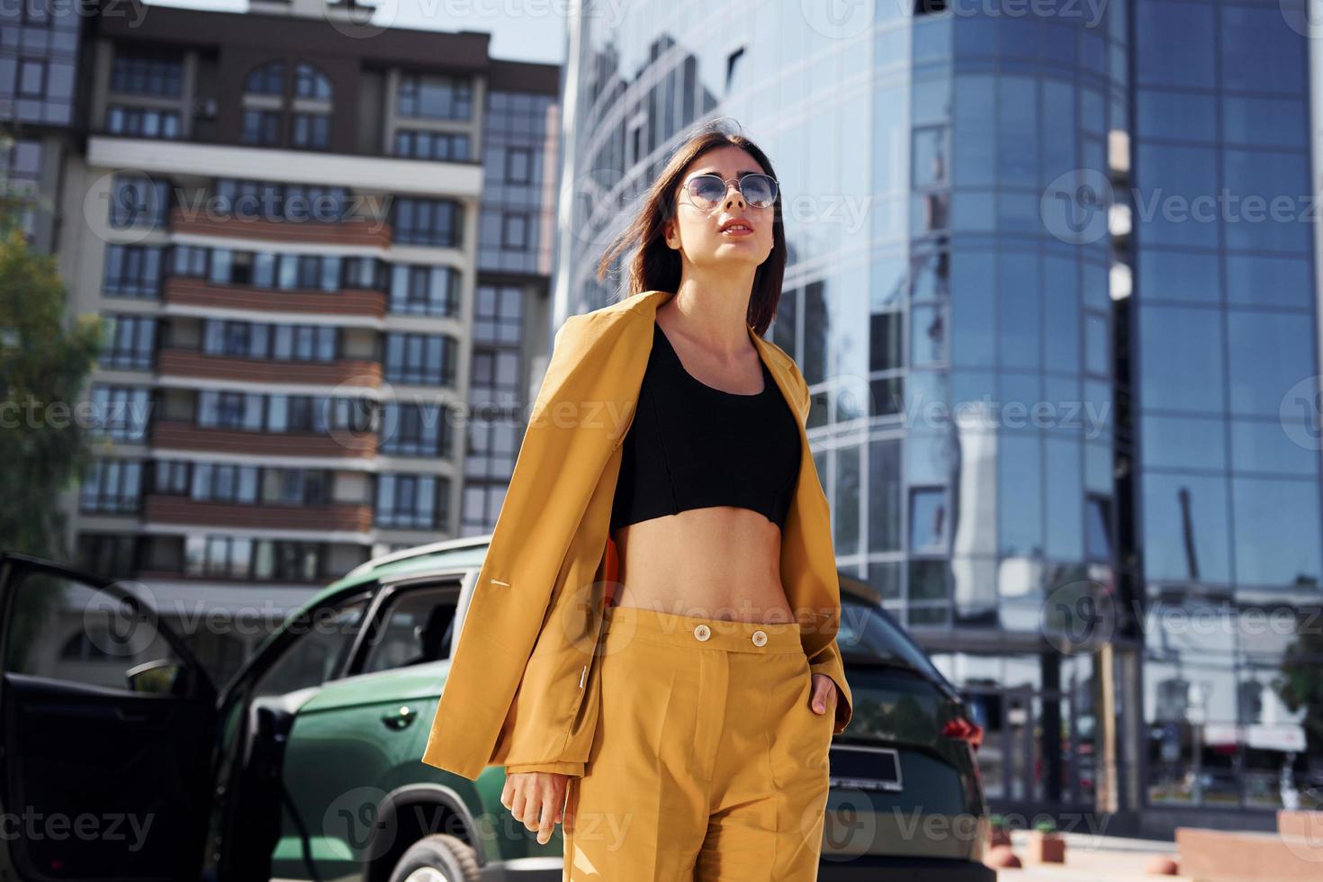 Walks forward from automobile. Young fashionable woman in burgundy colored coat at daytime with her car photo