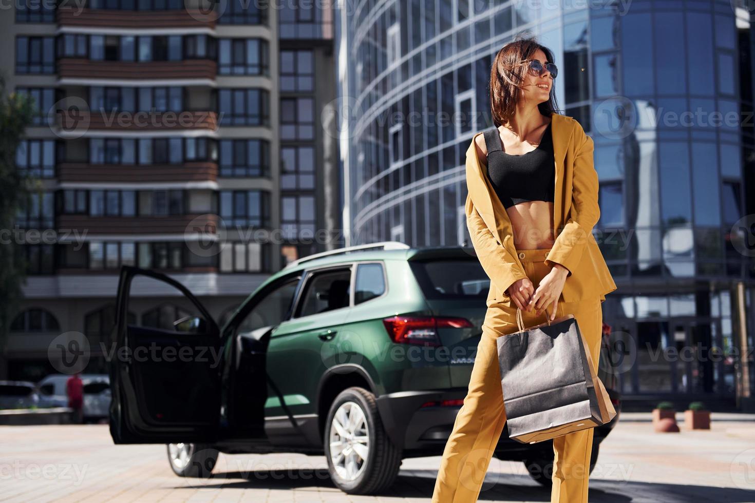 Modern business building at background. Young fashionable woman in burgundy colored coat at daytime with her car photo