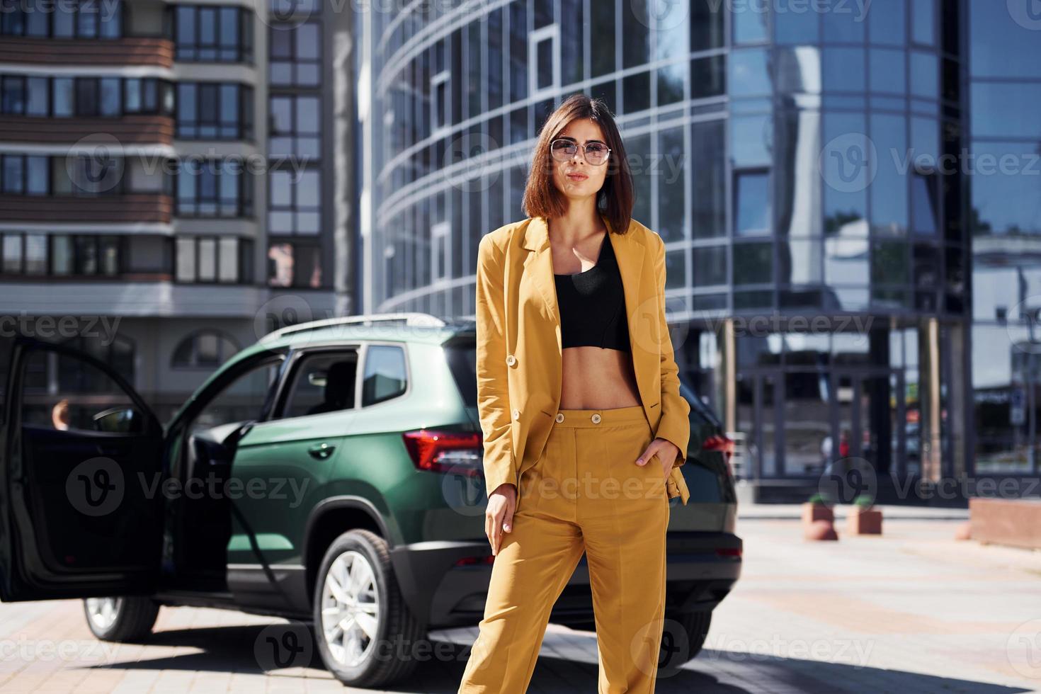 Modern business building at background. Young fashionable woman in burgundy colored coat at daytime with her car photo