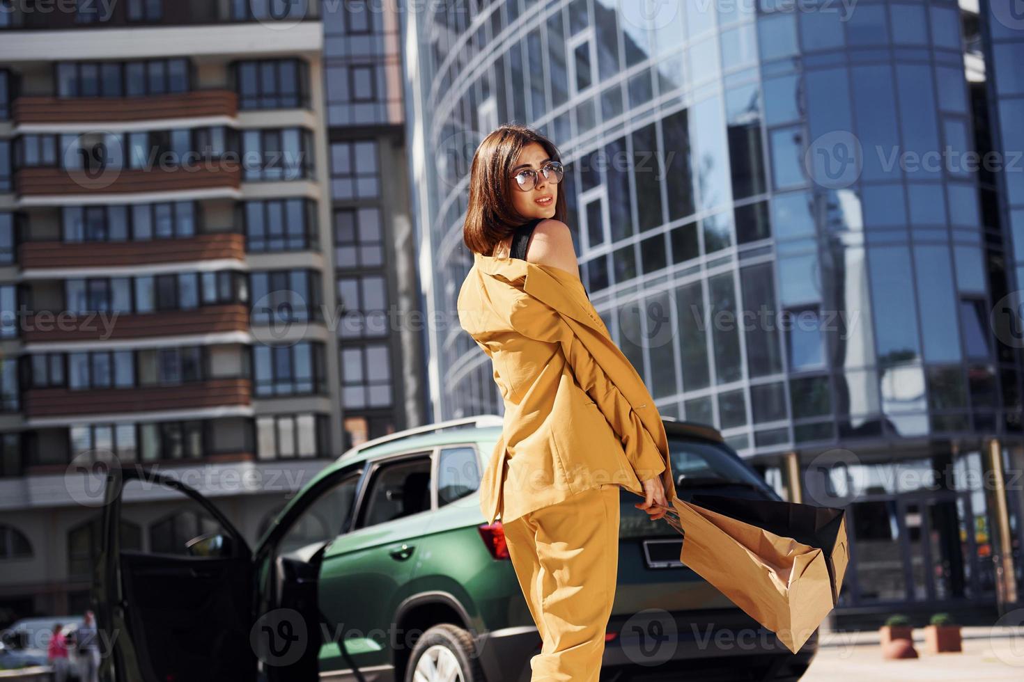 Modern business building at background. Young fashionable woman in burgundy colored coat at daytime with her car photo