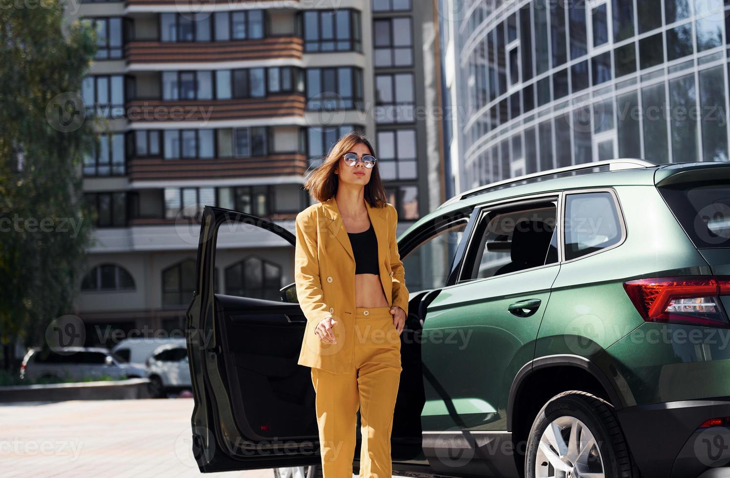 Walks forward from automobile. Young fashionable woman in burgundy colored coat at daytime with her car photo