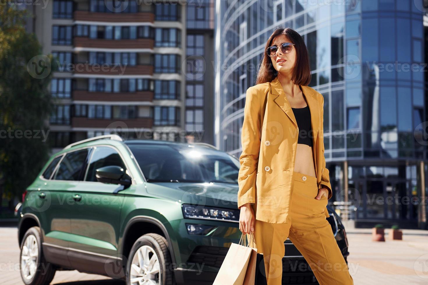 Young fashionable woman in burgundy colored coat at daytime with her car photo