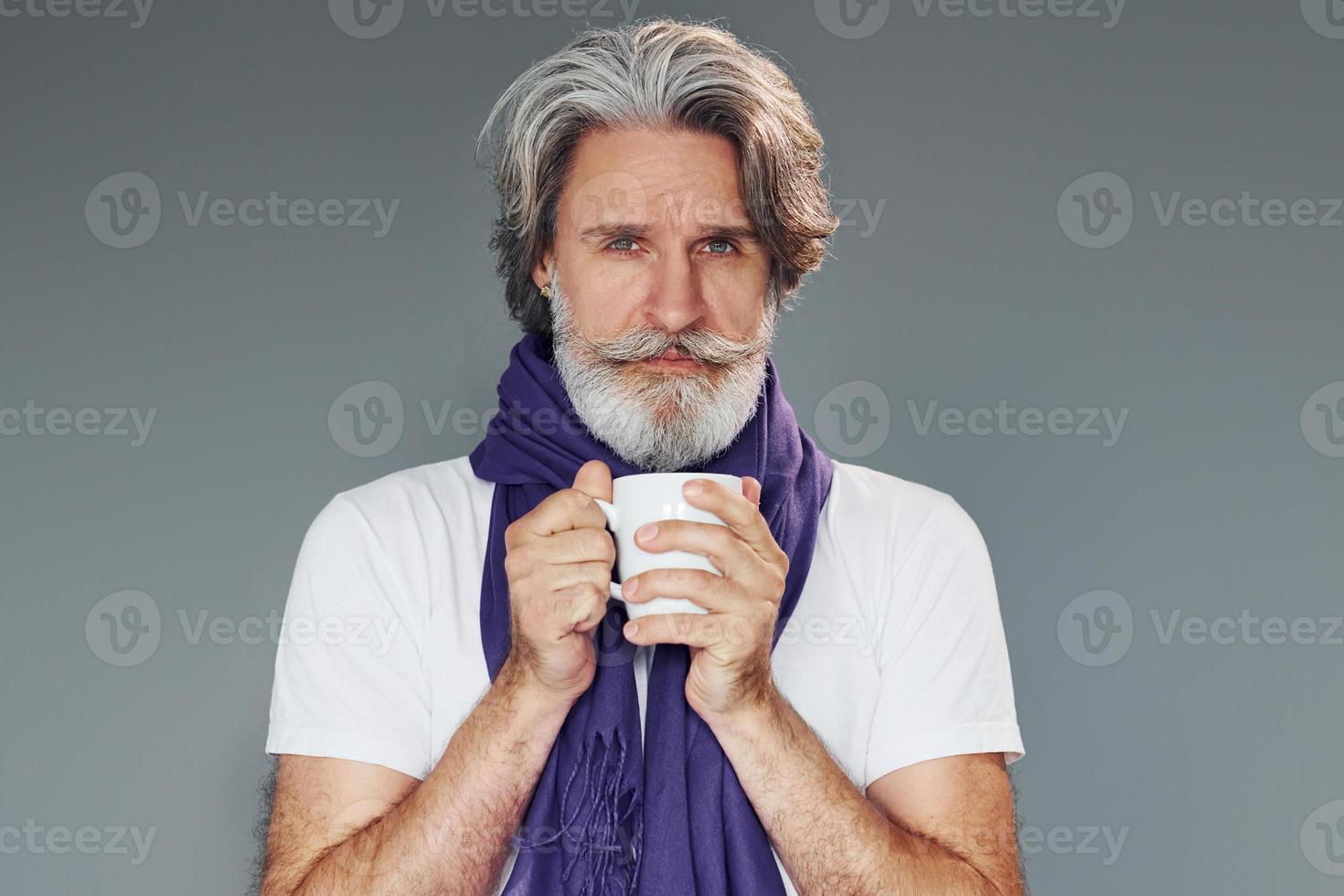 Getting sick. Against grey background. Stylish modern senior man with gray hair and beard is indoors photo