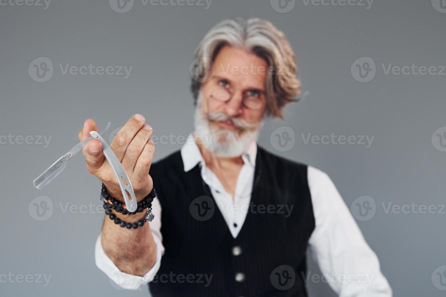 Barbershop tools. Against grey background. Stylish modern senior man with gray hair and beard is indoors photo
