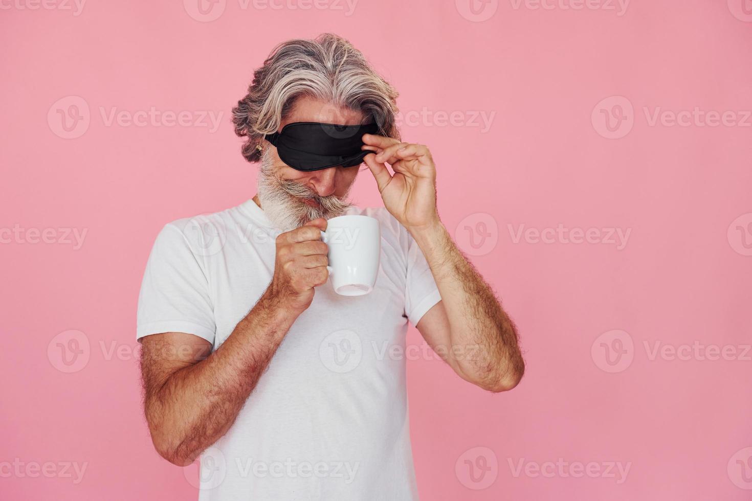 With sleep mask. Waking up. Stylish modern senior man with gray hair and beard is indoors photo