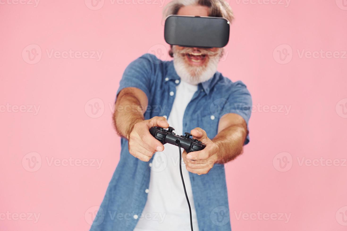 Playing game with virtual reality glasses and joystick. Stylish modern senior man with gray hair and beard is indoors photo