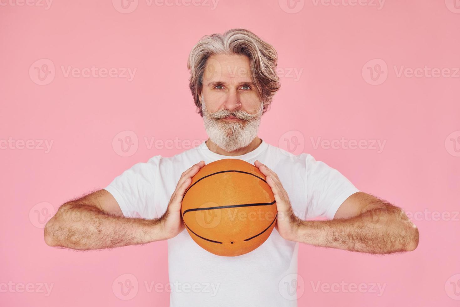 With sport ball in hands. Stylish modern senior man with gray hair and beard is indoors photo