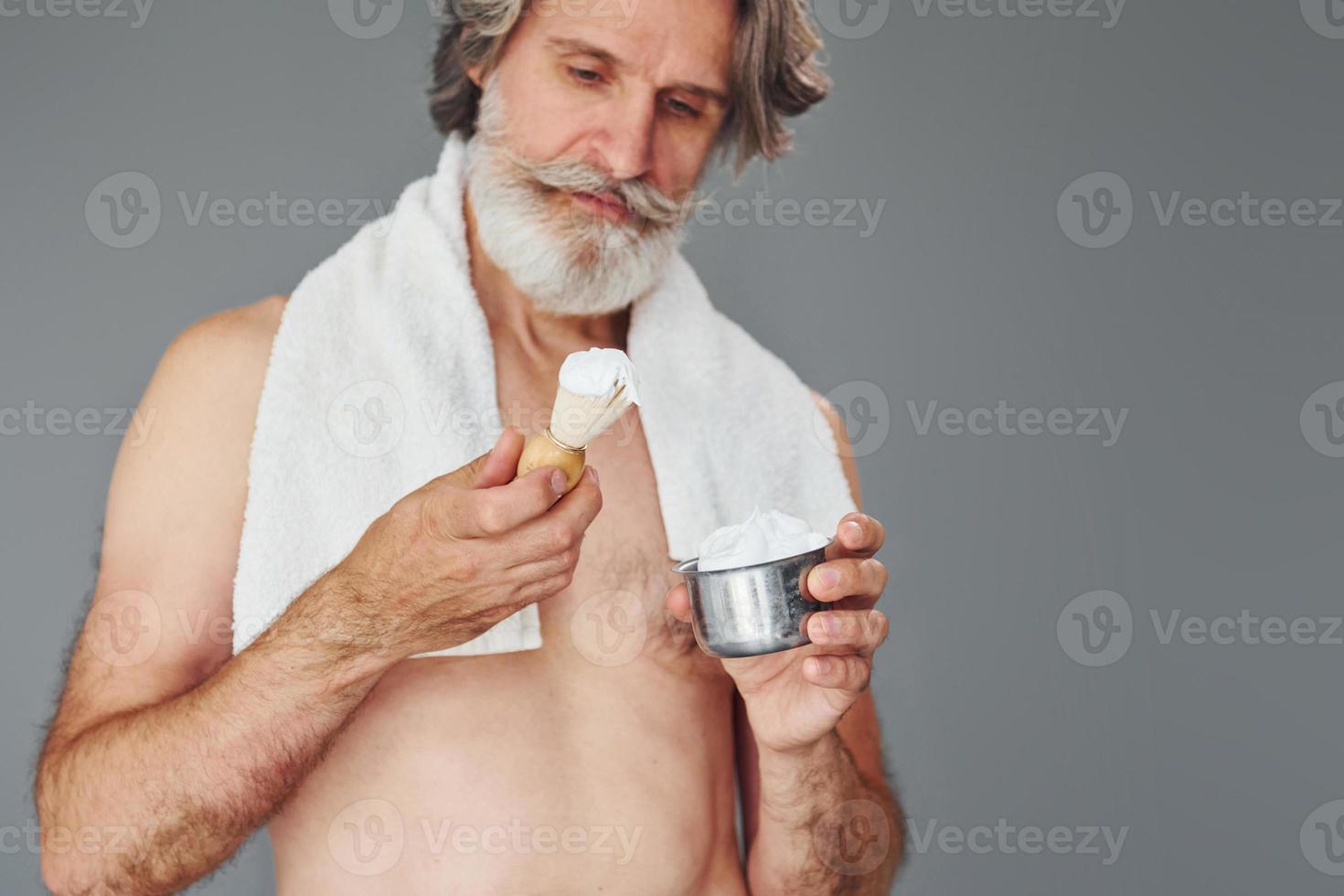 With shaving gel. Stylish modern senior man with gray hair and beard is indoors photo
