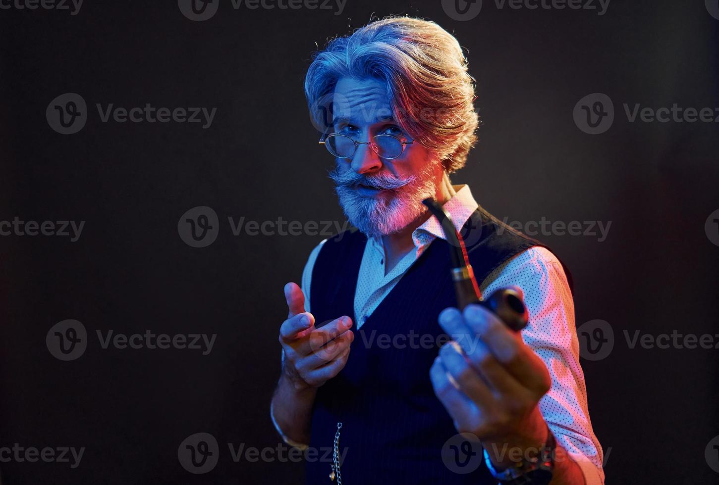 Smoking and having fun. Neon lighting. Stylish modern senior man with gray hair and beard is indoors photo