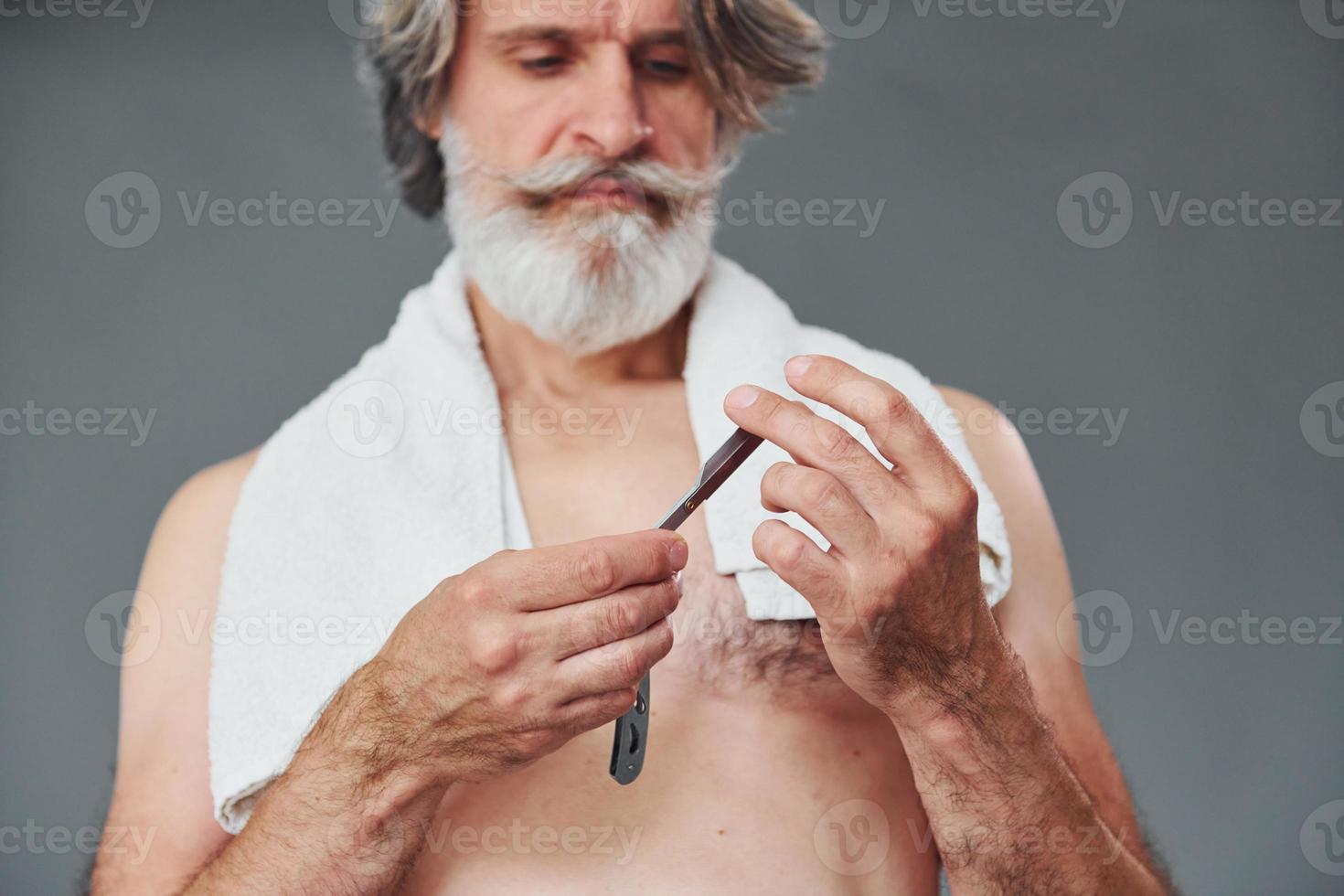 Taking care of beard. Stylish modern senior man with gray hair is indoors photo