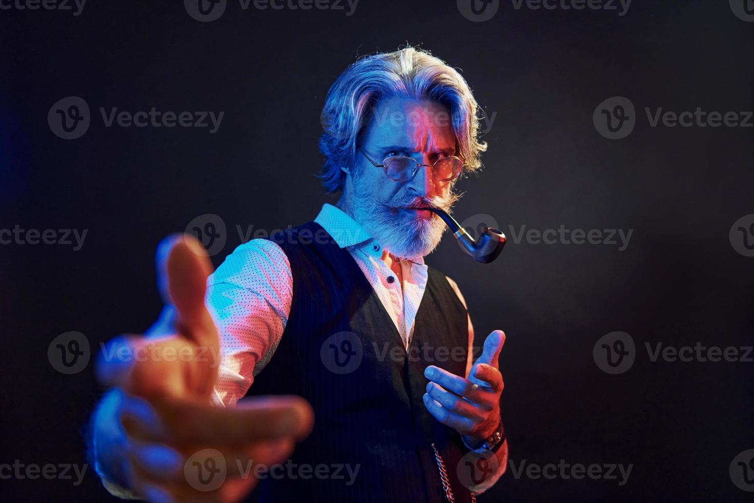 Smoking and having fun. Neon lighting. Stylish modern senior man with gray hair and beard is indoors photo