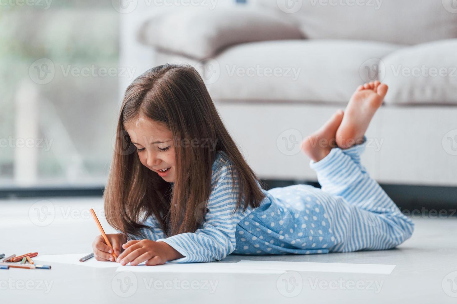 tirado en el suelo y dibujando. linda niña adentro en casa sola foto