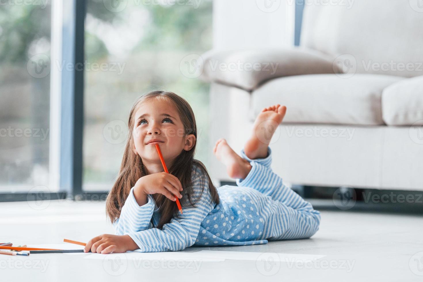 Lying on the floor and drawing. Cute little girl indoors at home alone photo