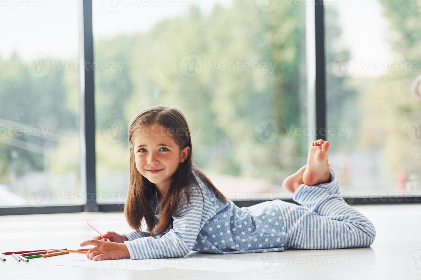 Lying on the floor and drawing. Cute little girl indoors at home alone photo