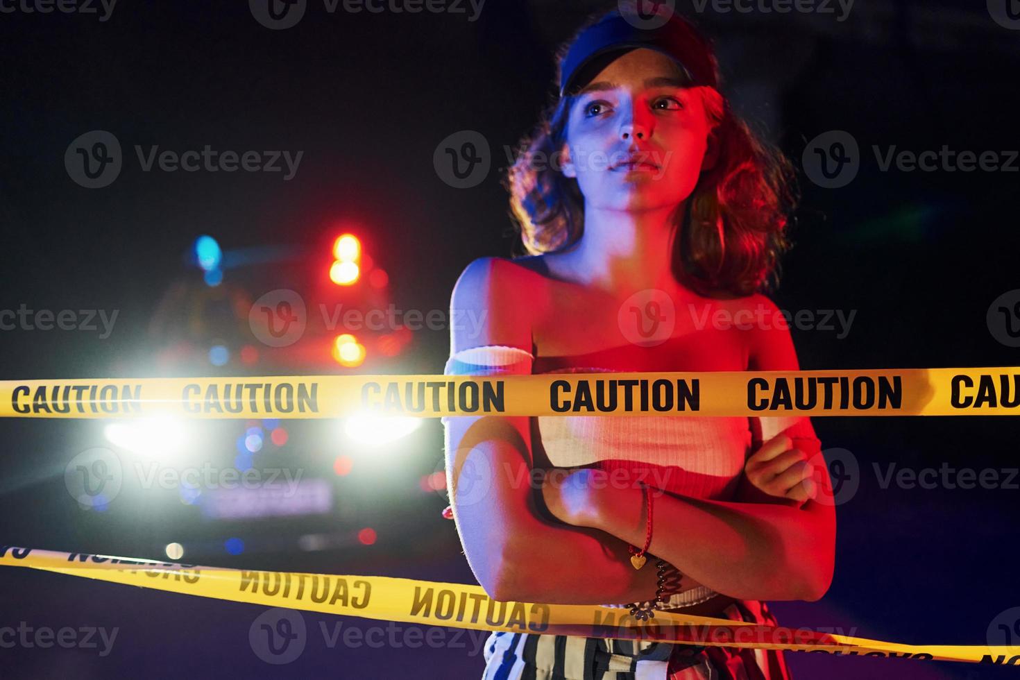 Cute young girl with curly hair and in hat standing outdoors near police line tape. Conception of crime or riot photo