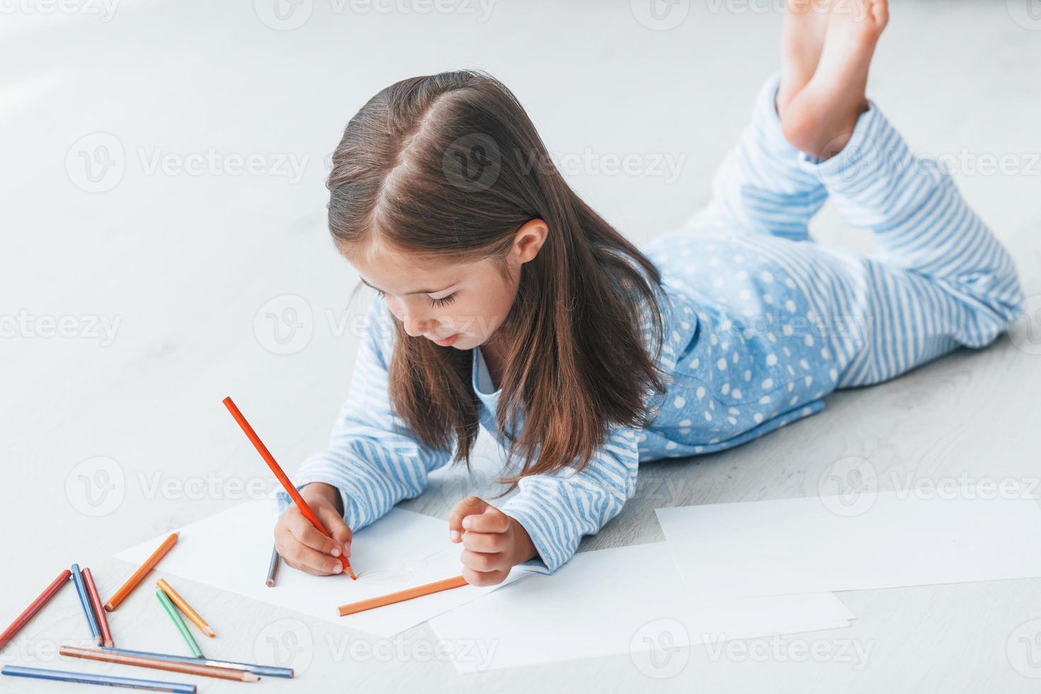 Lying on the floor and drawing. Cute little girl indoors at home alone photo