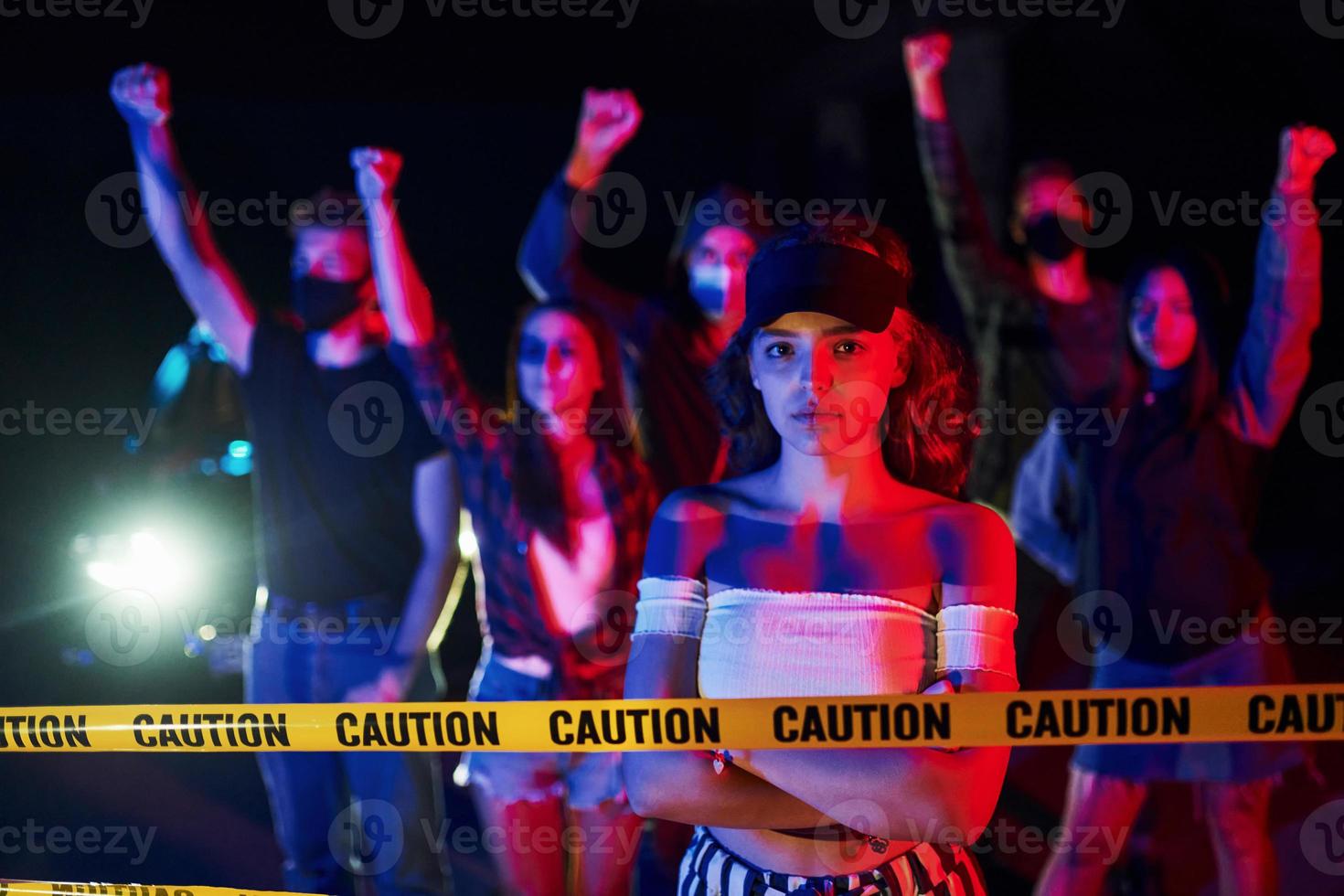 Calm woman standing in front of crowd. Group of protesting young people that standing together. Activist for human rights or against government photo