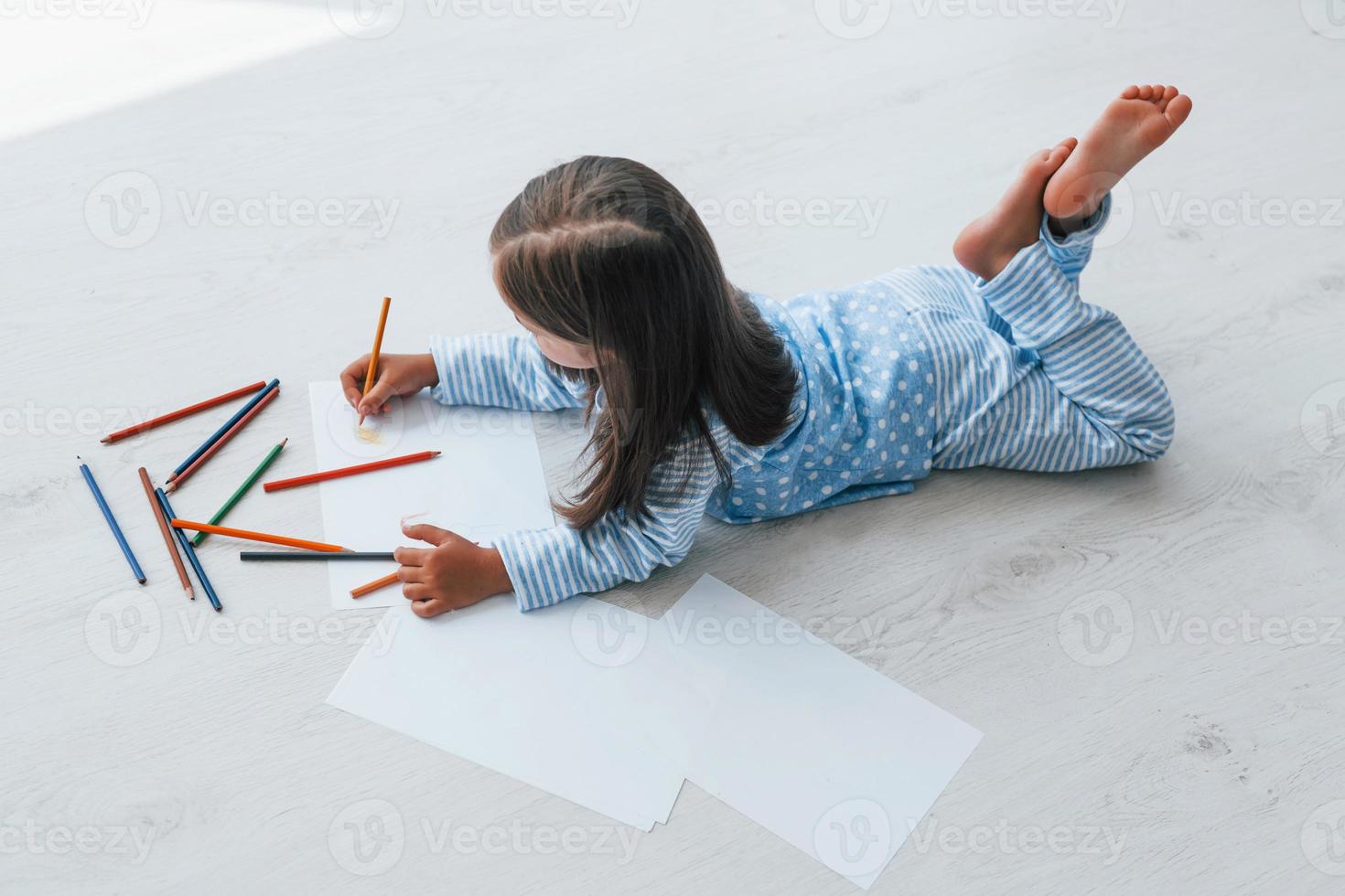 Lying on the floor and drawing. Cute little girl indoors at home alone photo