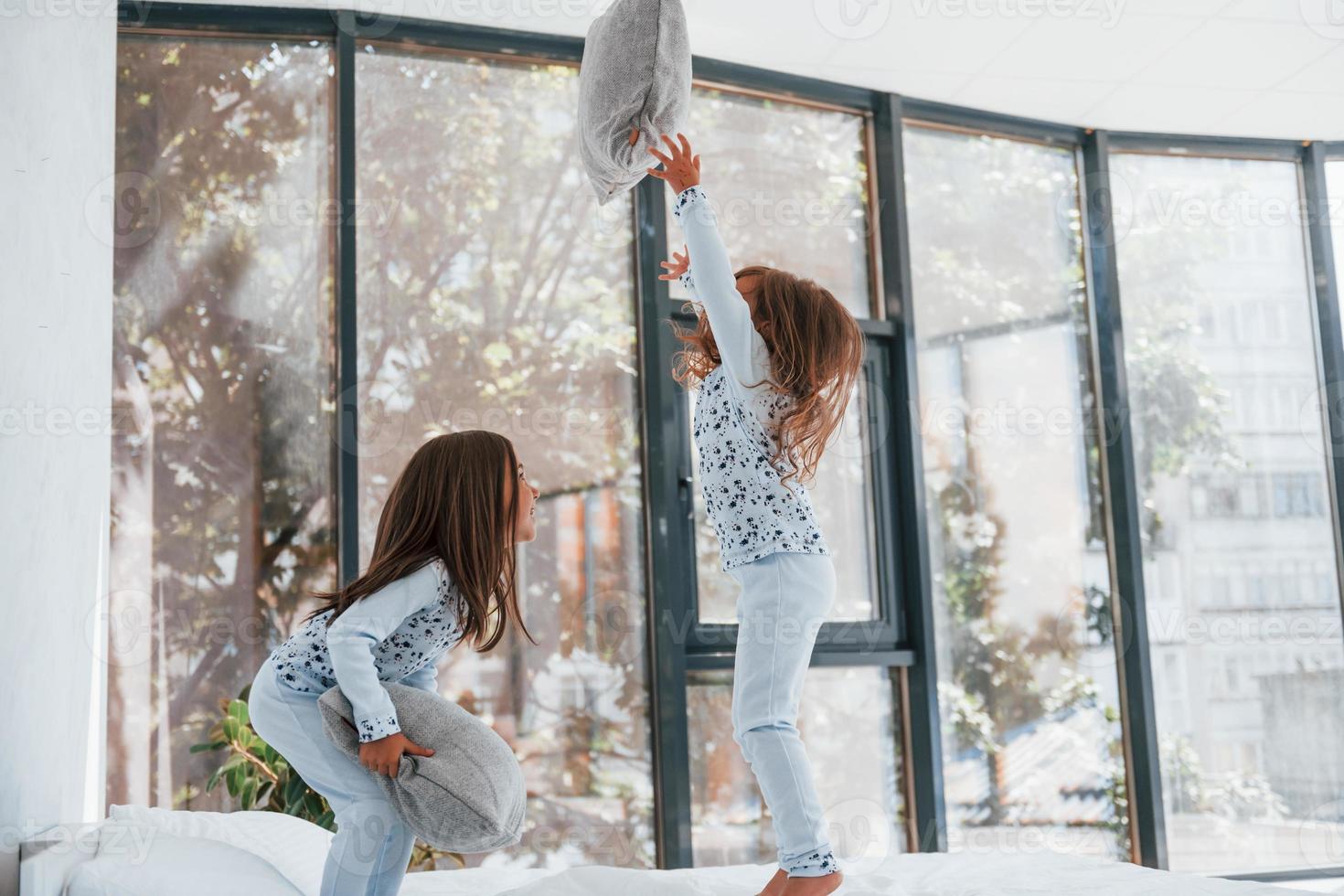 With pillows in hands. Two cute little girls indoors at home together. Children having fun photo