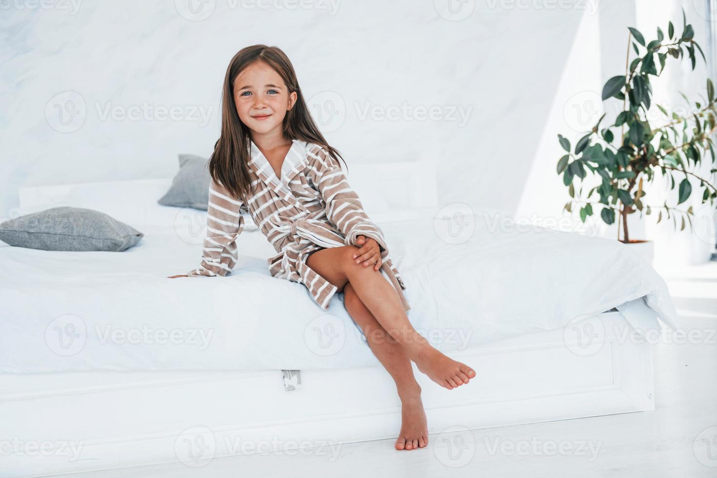 Cute little girl indoors sitting on the sofa at daytime in casual clothes photo