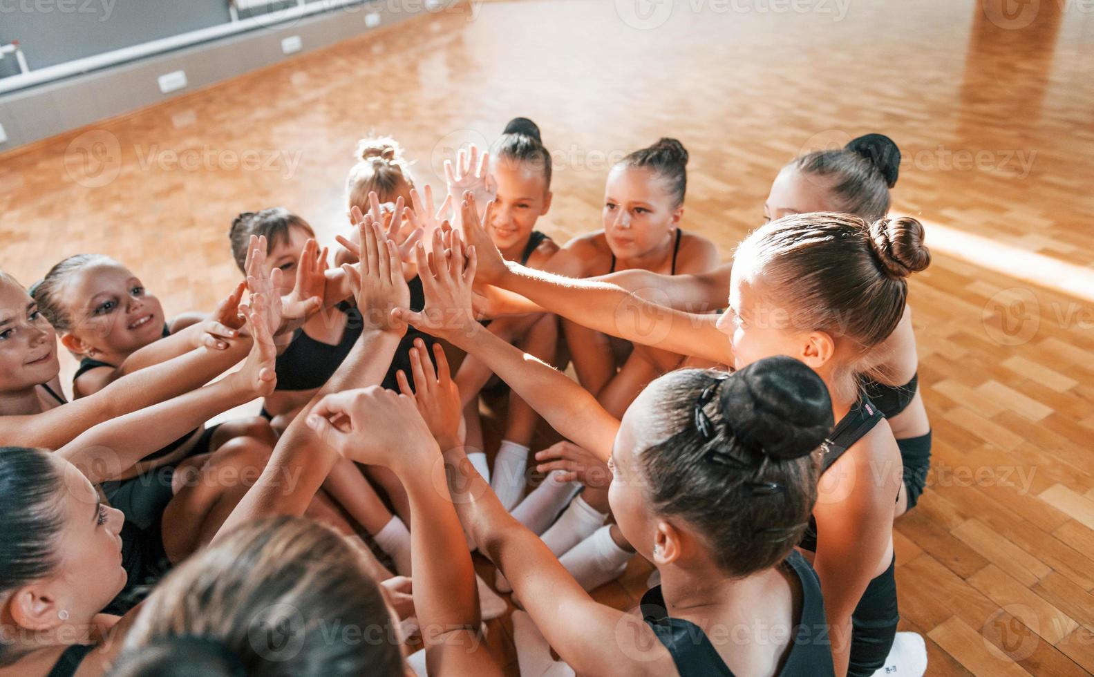 Many of people. Group of female kids practicing athletic exercises together indoors photo