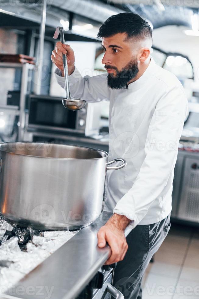 Cooks delicious soup. Chef in white uniform cooking food at kitchen. Busy day at work photo