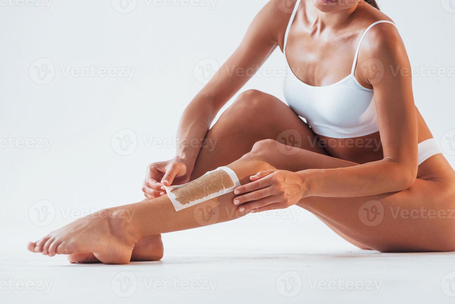 Removing hair that on leg. Beautiful woman with slim body in underwear is in the studio photo