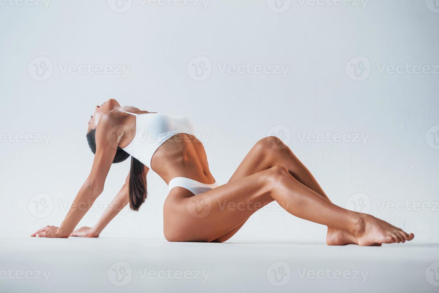 Sitting on the floor. Beautiful woman with slim body in underwear is in the studio photo