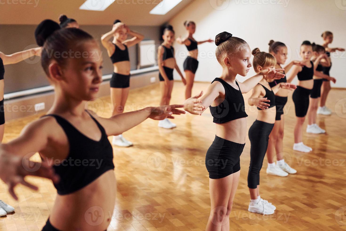 Standing in the row. Group of female kids practicing athletic exercises together indoors photo