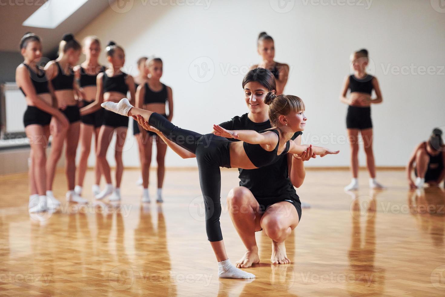 Woman teaching and helping. Group of female kids practicing athletic exercises together indoors photo
