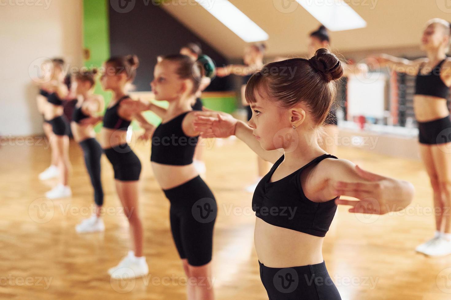 Standing in the row. Group of female kids practicing athletic exercises together indoors photo
