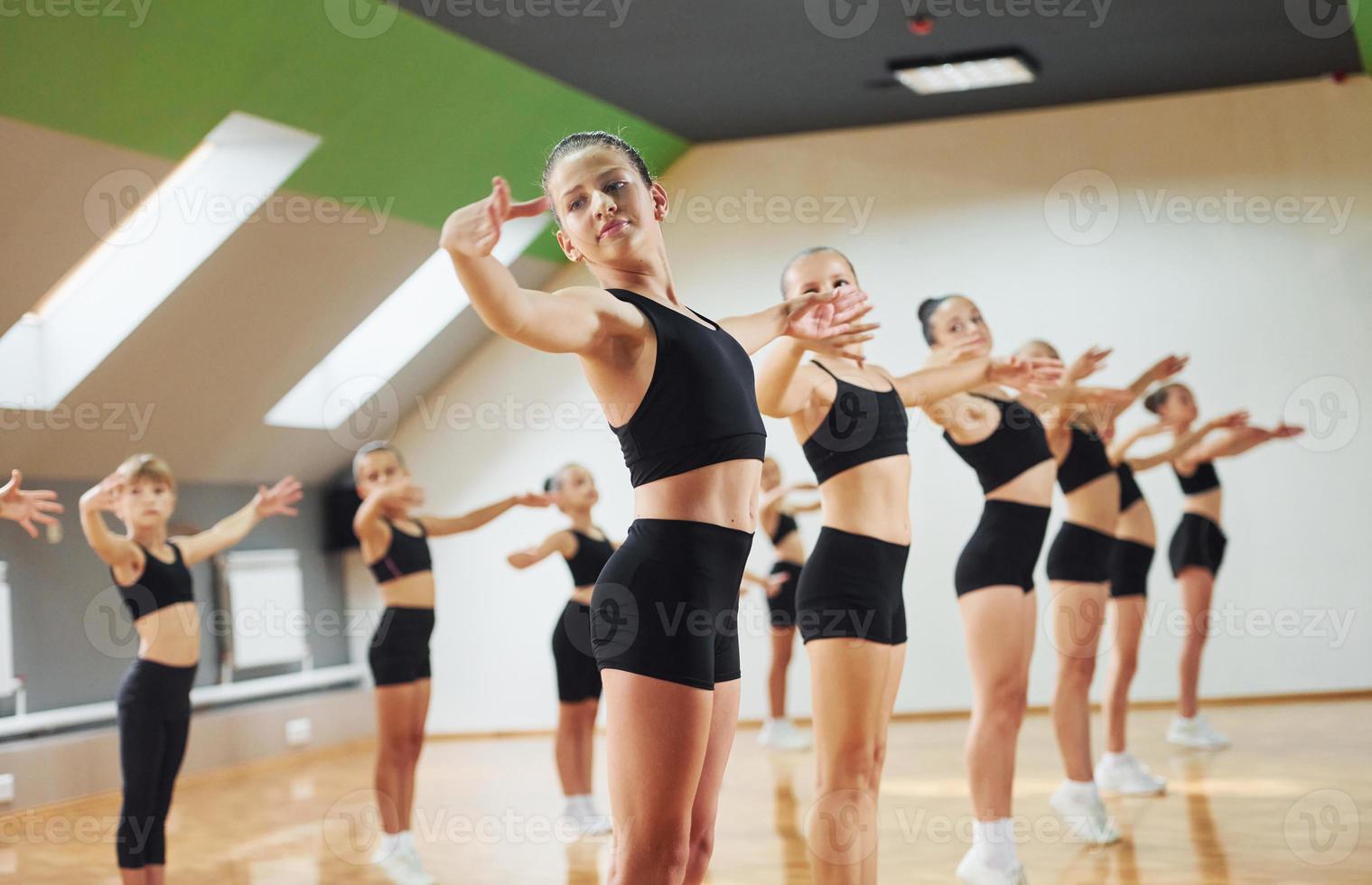 Standing and doing synchronised moves. Group of female kids practicing athletic exercises together indoors photo