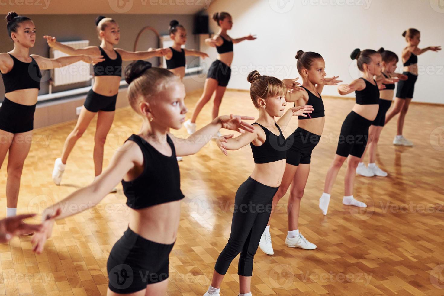 Standing in the row. Group of female kids practicing athletic exercises together indoors photo