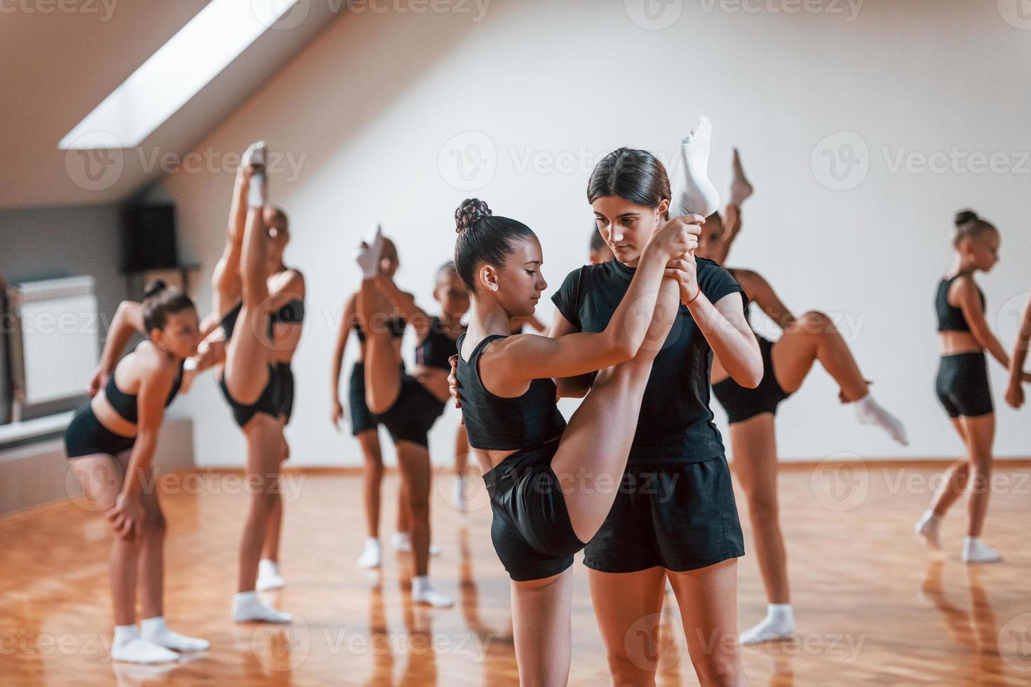 With help from coach. Group of female kids practicing athletic exercises together indoors photo