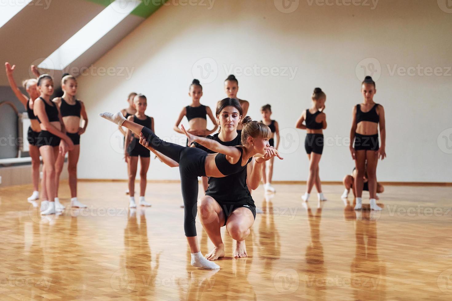 With help from coach. Group of female kids practicing athletic exercises together indoors photo