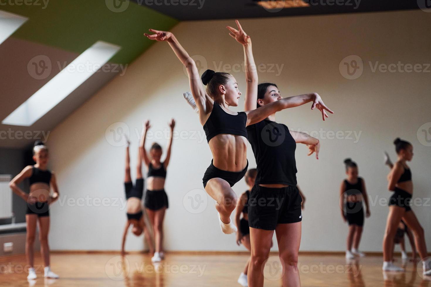 Woman teaching and helping. Group of female kids practicing athletic exercises together indoors photo