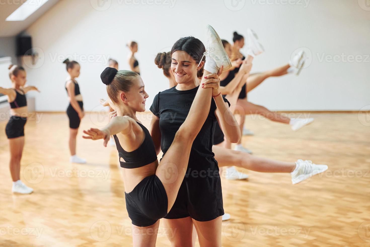 Learning from coach. Group of female kids practicing athletic exercises together indoors photo