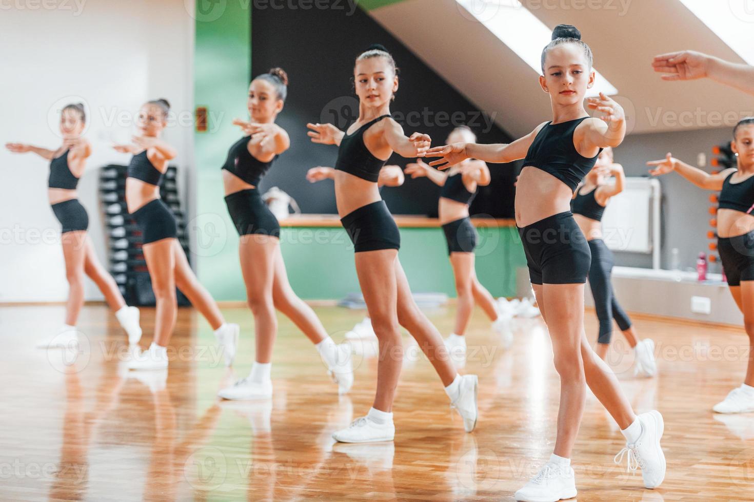 Standing and doing synchronised moves. Group of female kids practicing athletic exercises together indoors photo